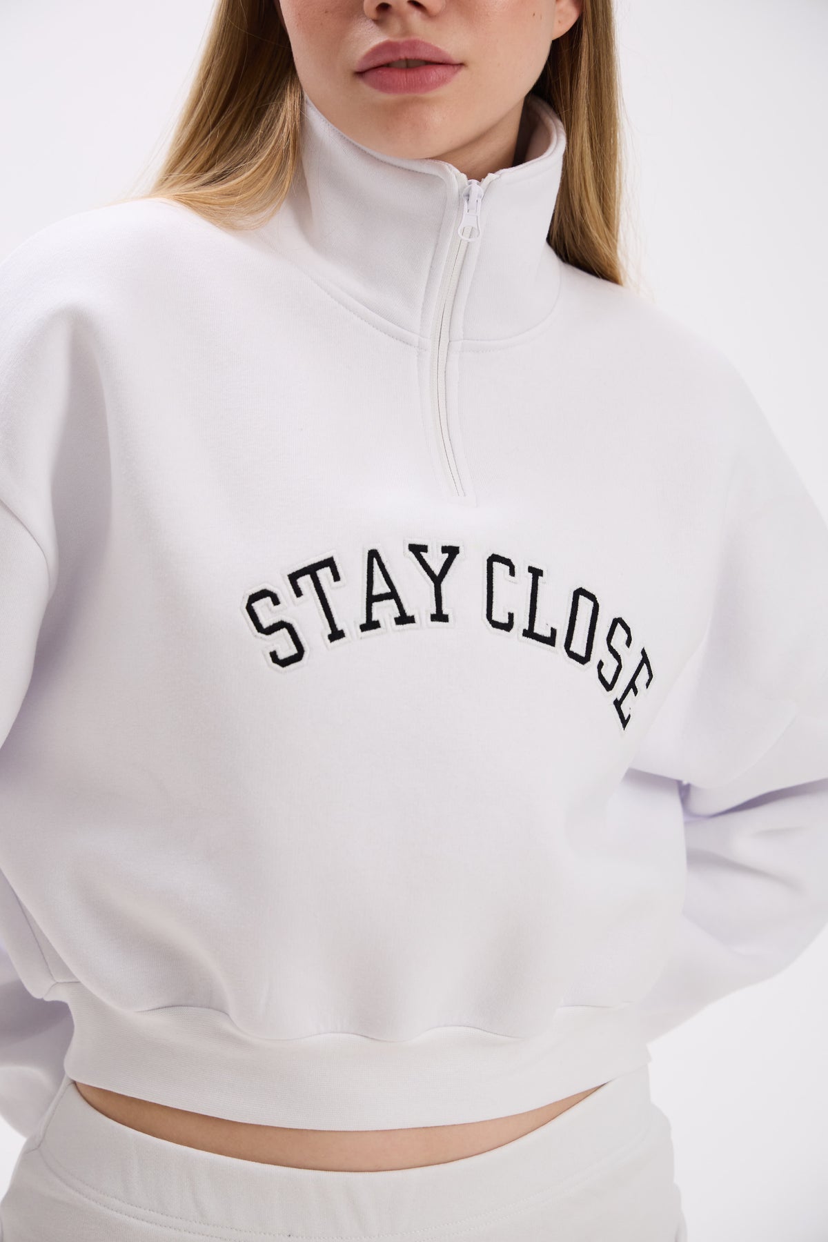 White cropped half-zip hoodie featuring bold black 'STAY CLOSE' chest embroidery – close-up detail shot on plain background