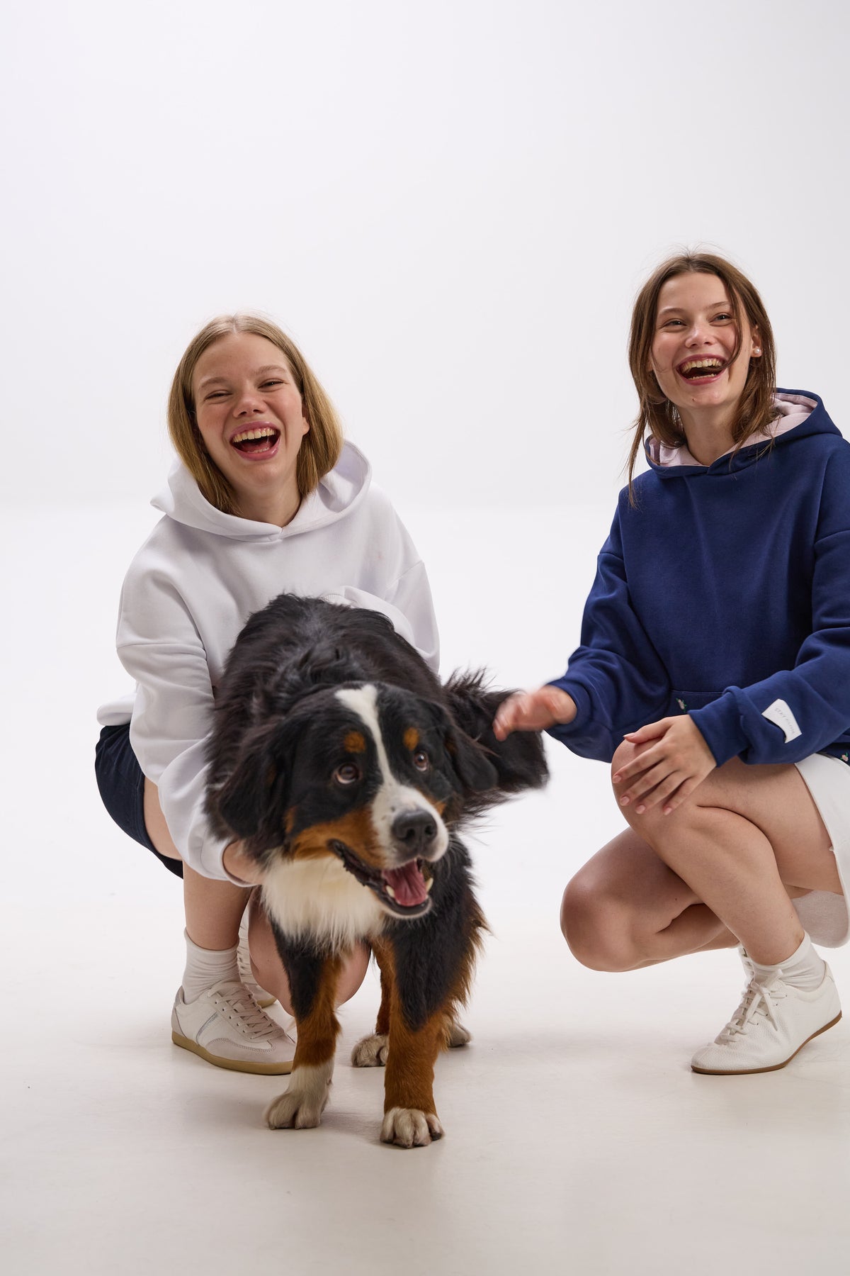 Two people in hoodies with a dog on a white background.