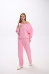 Model wearing a pink loungewear set with an off-shoulder oversized sweatshirt and straight-leg sweatpants, styled with white sneakers.