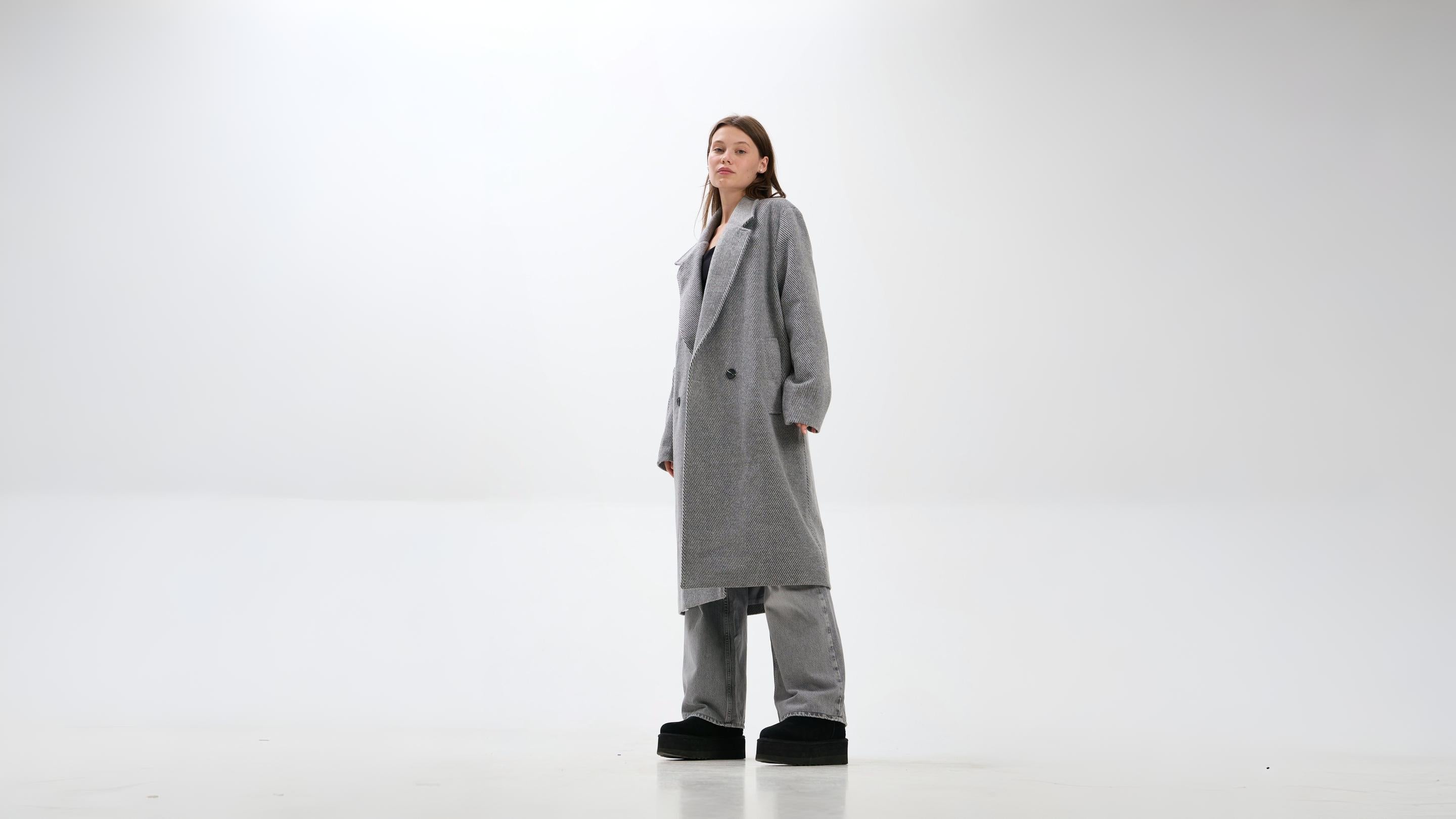 Person wearing a long gray coat on a white background.