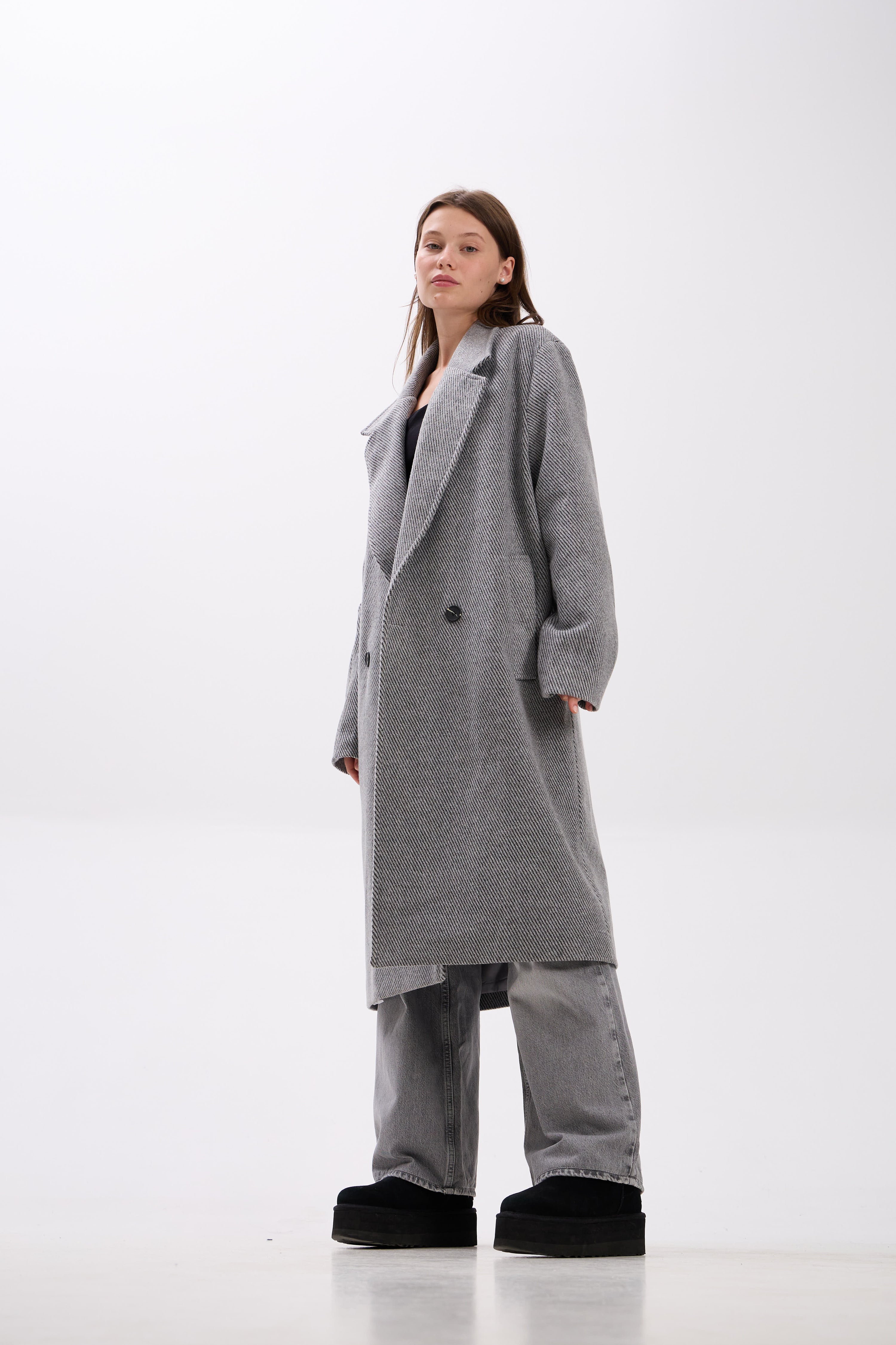 Person wearing a long gray coat on a white background.