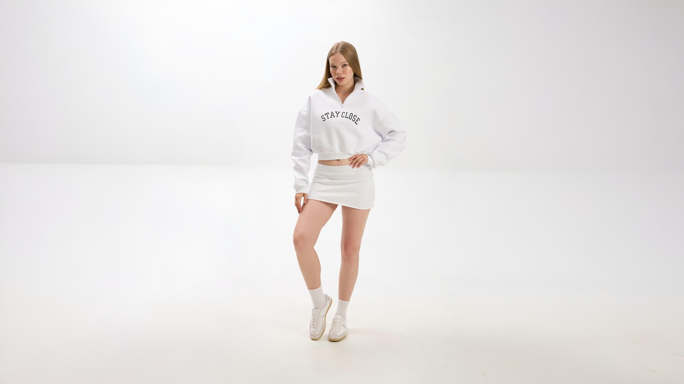 Person wearing a white hoodie and skirt set on a plain background.