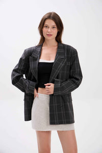 Woman wearing a black pinstripe blazer over a black top and white skirt on a white background.