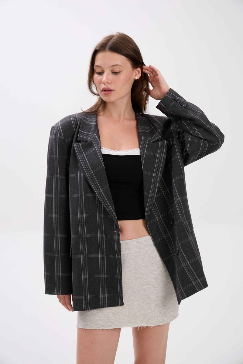 Woman wearing a black checkered blazer over a black top and white skirt on a white background.