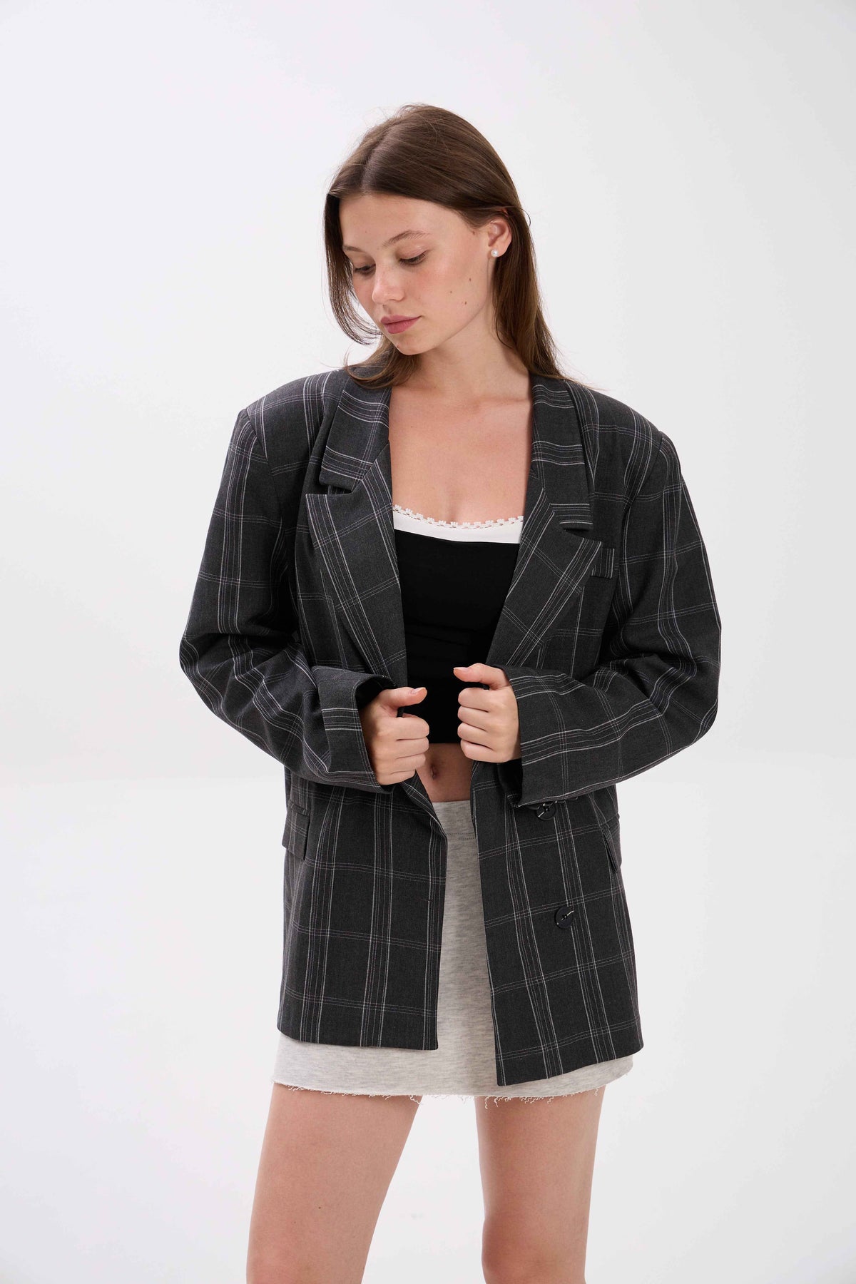 Woman wearing a black checkered blazer over a black top and white skirt on a white background.