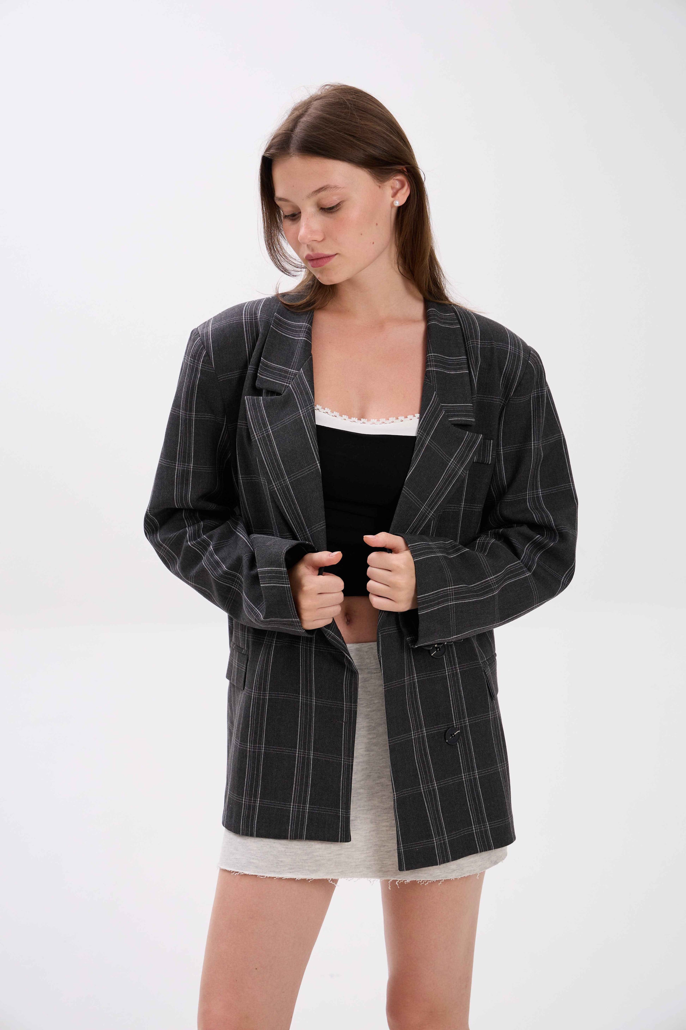 Woman wearing a black checkered blazer over a black top and white skirt on a white background.