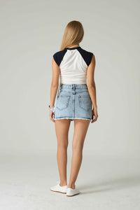 Woman wearing a white and black sleeveless top with a denim skirt on a plain background.