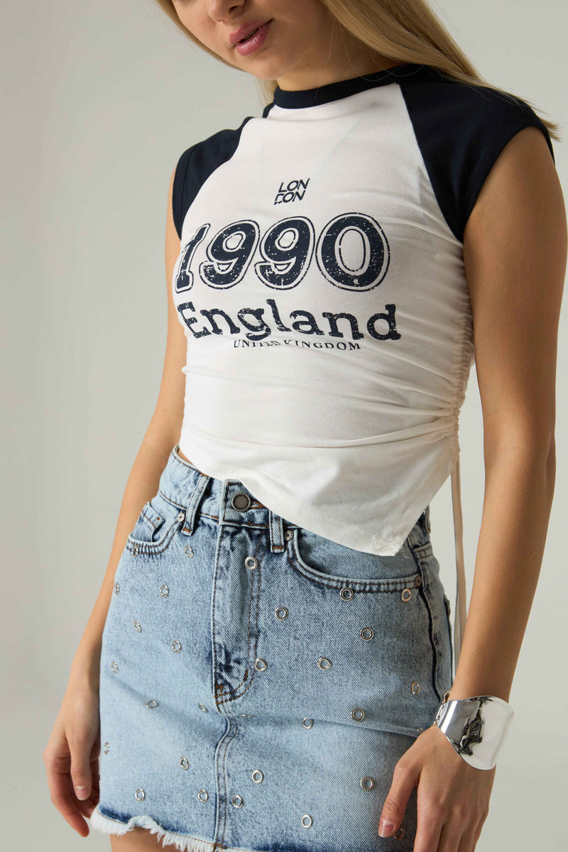 Person wearing a white and black '1990 England' t-shirt with a denim skirt.