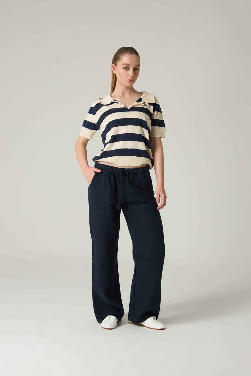 Woman wearing a striped shirt and dark pants on a plain background.