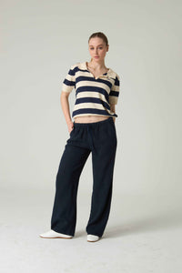 Woman wearing a striped shirt and dark pants on a plain background.