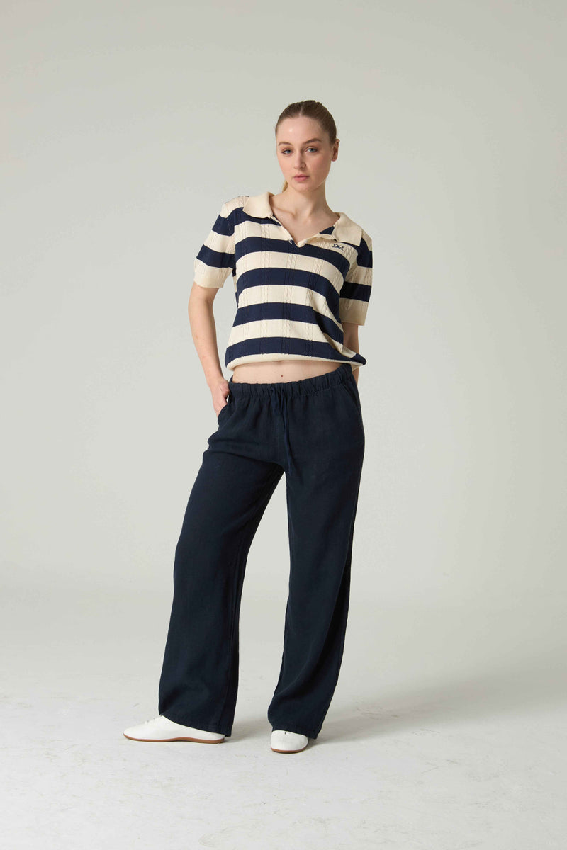 Woman wearing a striped shirt and dark pants on a plain background.