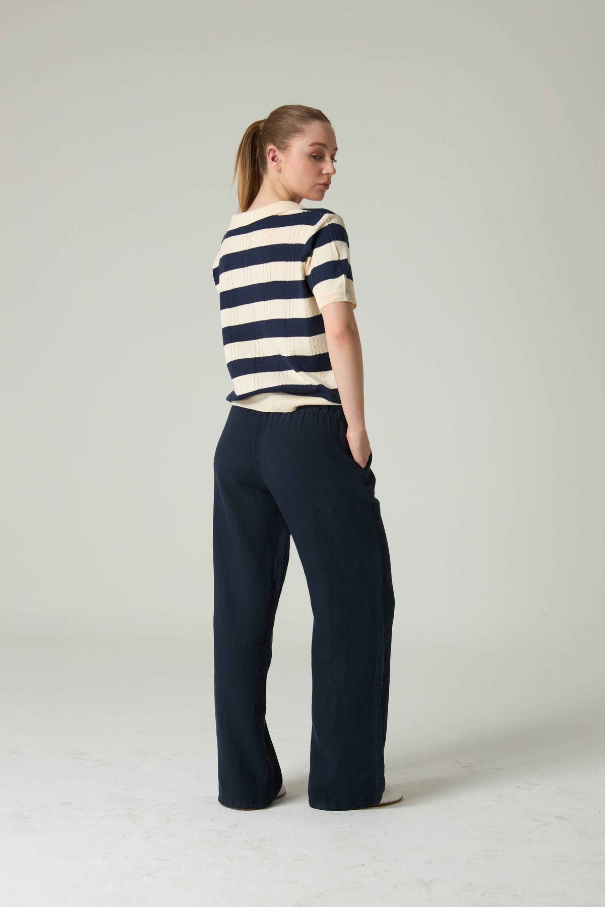 Woman wearing a striped shirt and dark pants on a plain background.