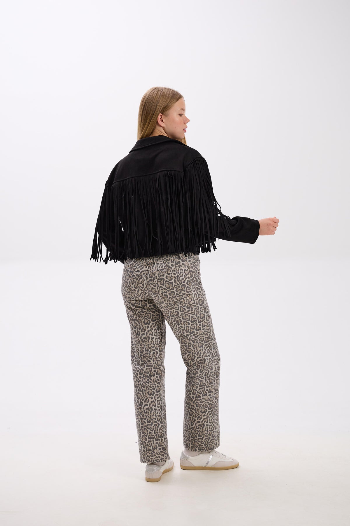 Person wearing a black fringe jacket and patterned pants on a white background.
