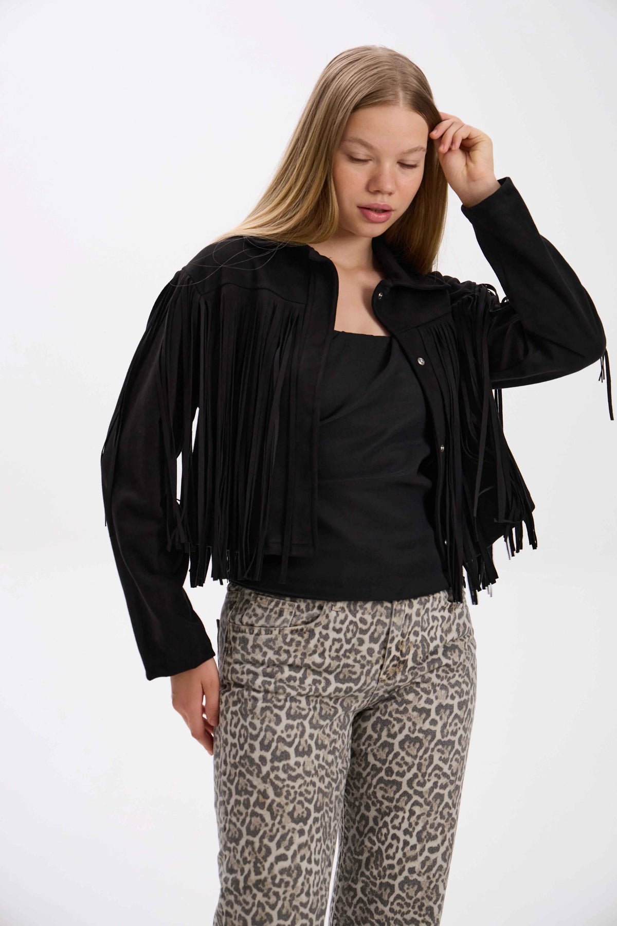 Woman wearing a black fringe jacket, black top, and leopard print pants on a white background.