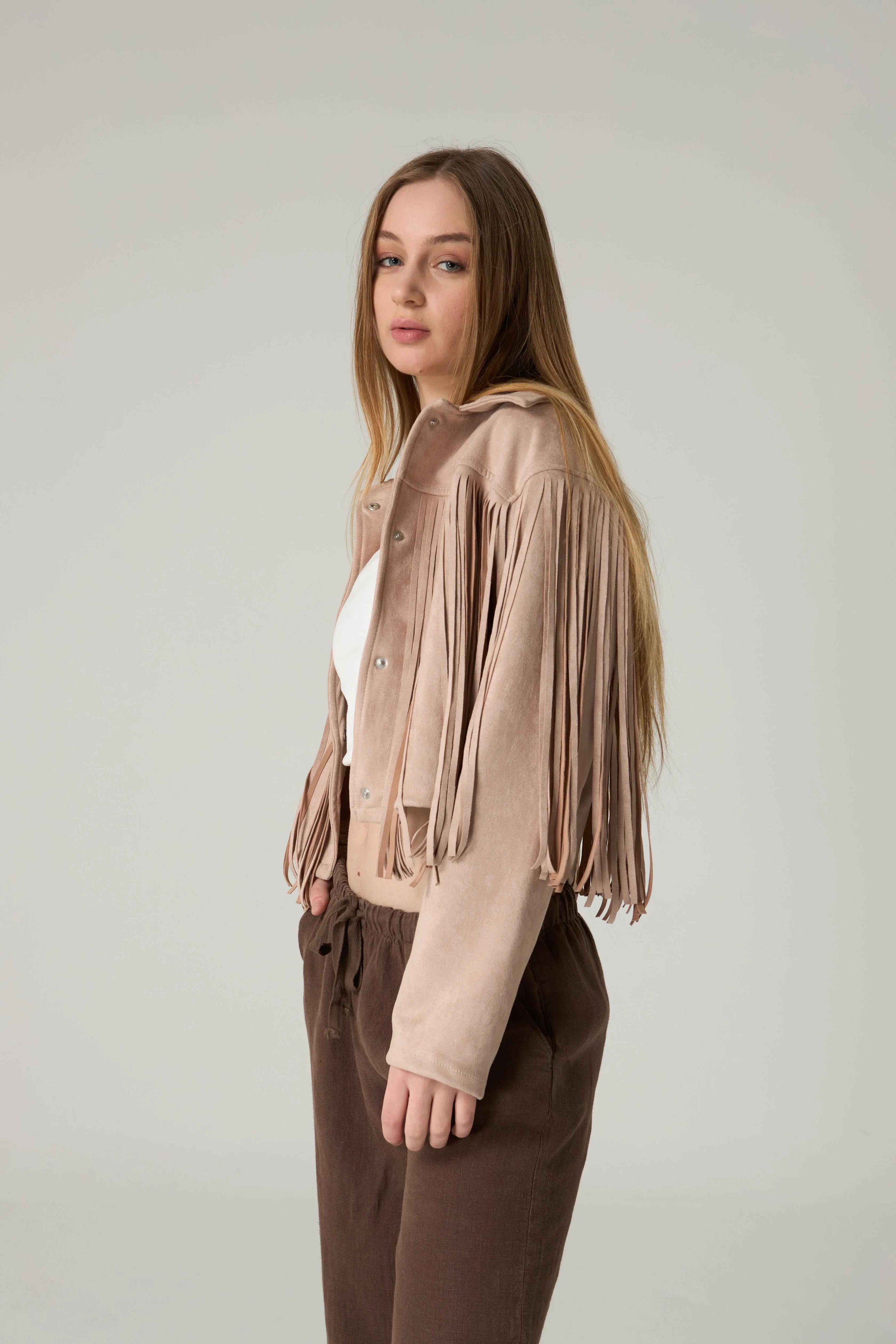 Woman wearing a beige fringe jacket and brown pants against a plain background.