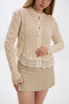 Woman wearing a beige lace cardigan over a beige skirt on a white background.