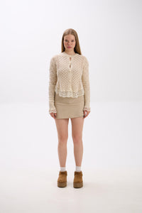 Woman wearing a beige knitted sweater and skirt with brown boots on a white background.