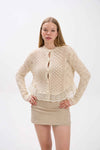 Woman wearing a beige lace cardigan over a beige dress on a white background.