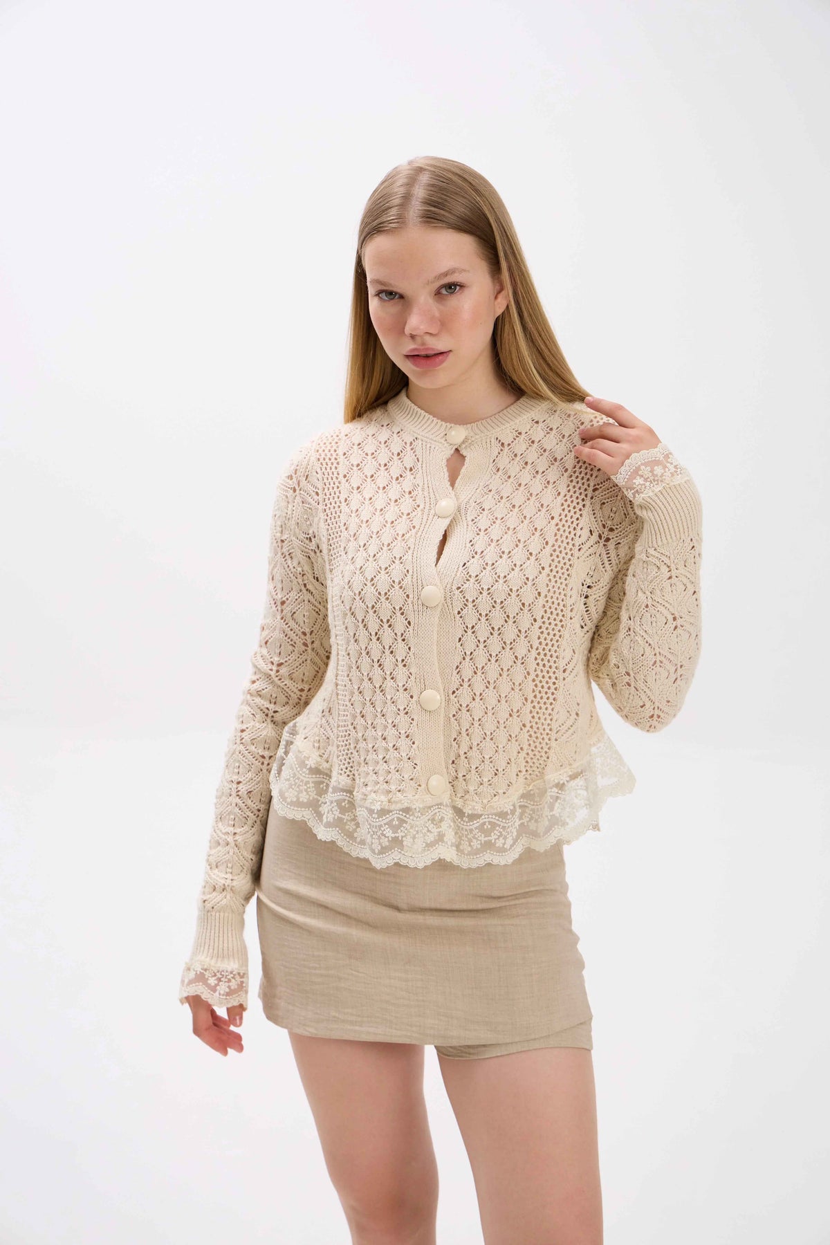 Woman wearing a beige lace top and skirt on a white background.