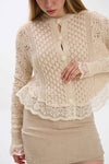 Woman wearing a beige knitted cardigan with lace details on a white background.