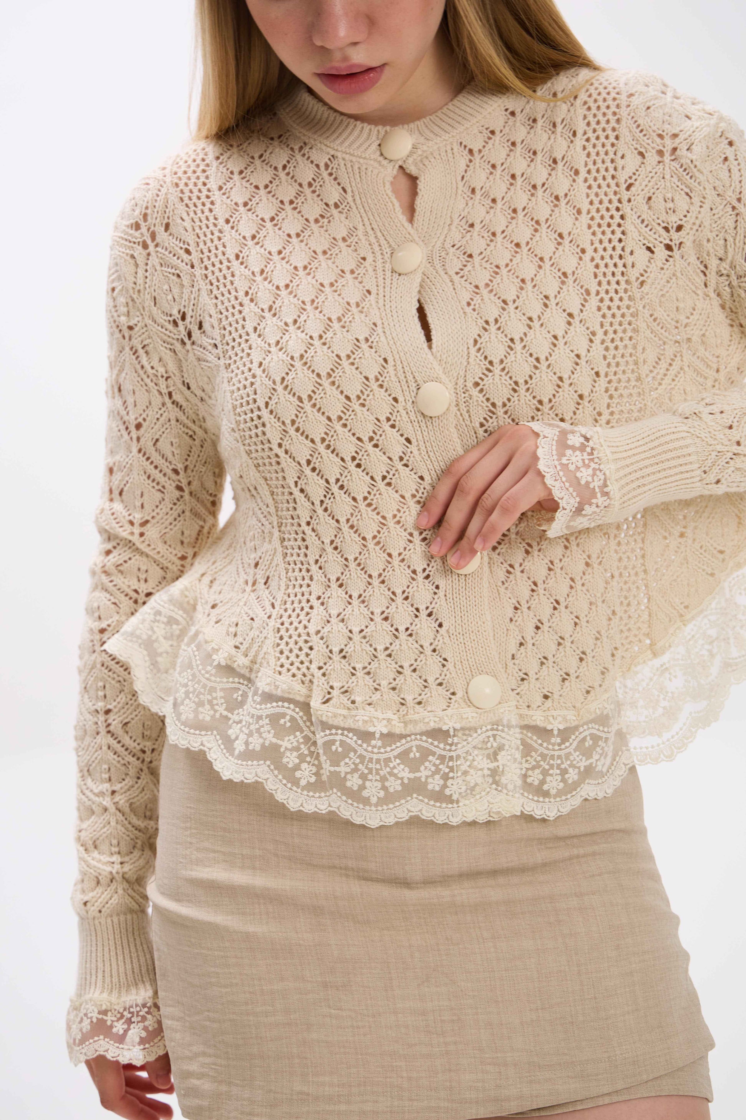 Woman wearing a beige knitted cardigan with lace details on a white background.