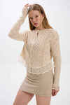 Woman wearing a beige lace cardigan over a matching skirt on a white background.