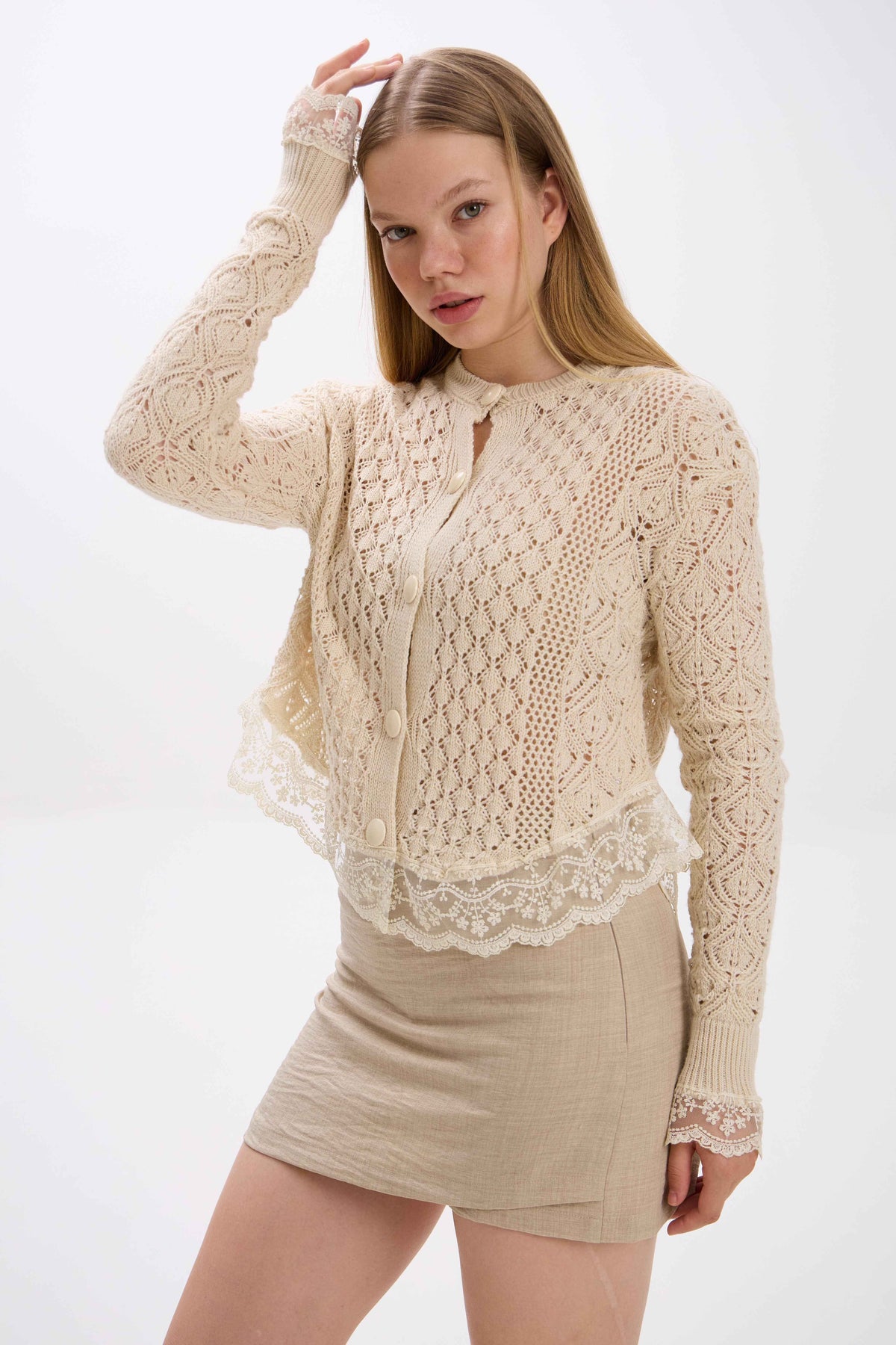 Woman wearing a beige lace cardigan over a matching skirt on a white background.