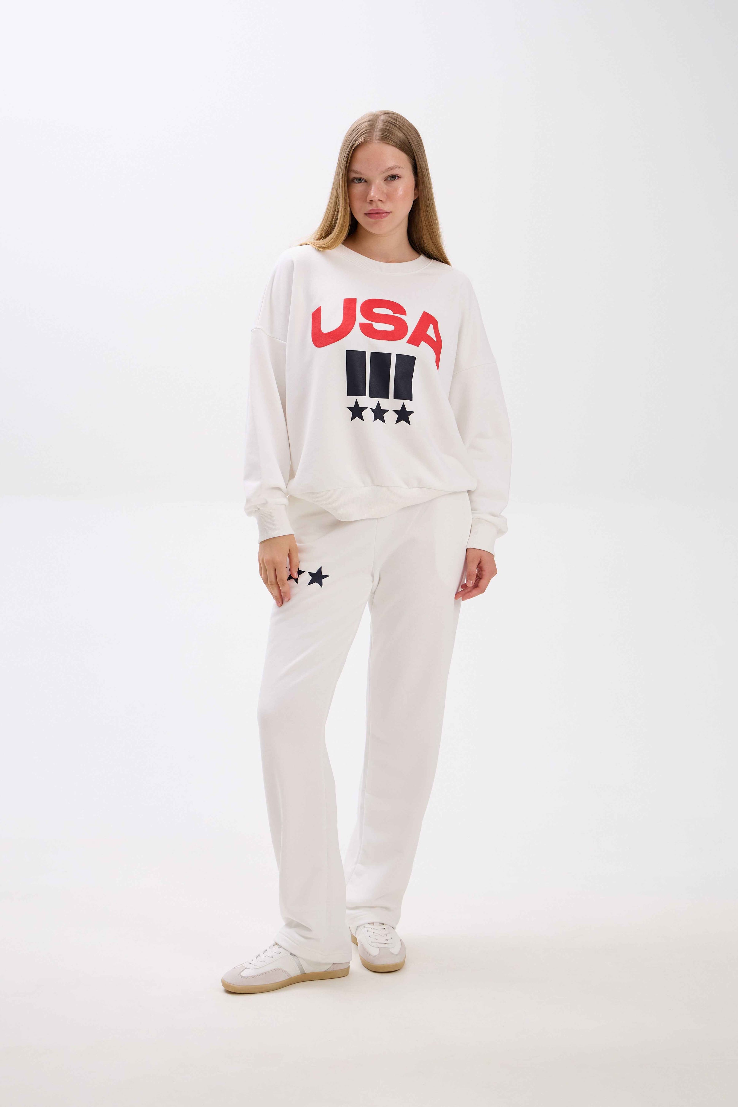 Person wearing a white sweatshirt with 'USA' text on a plain background.