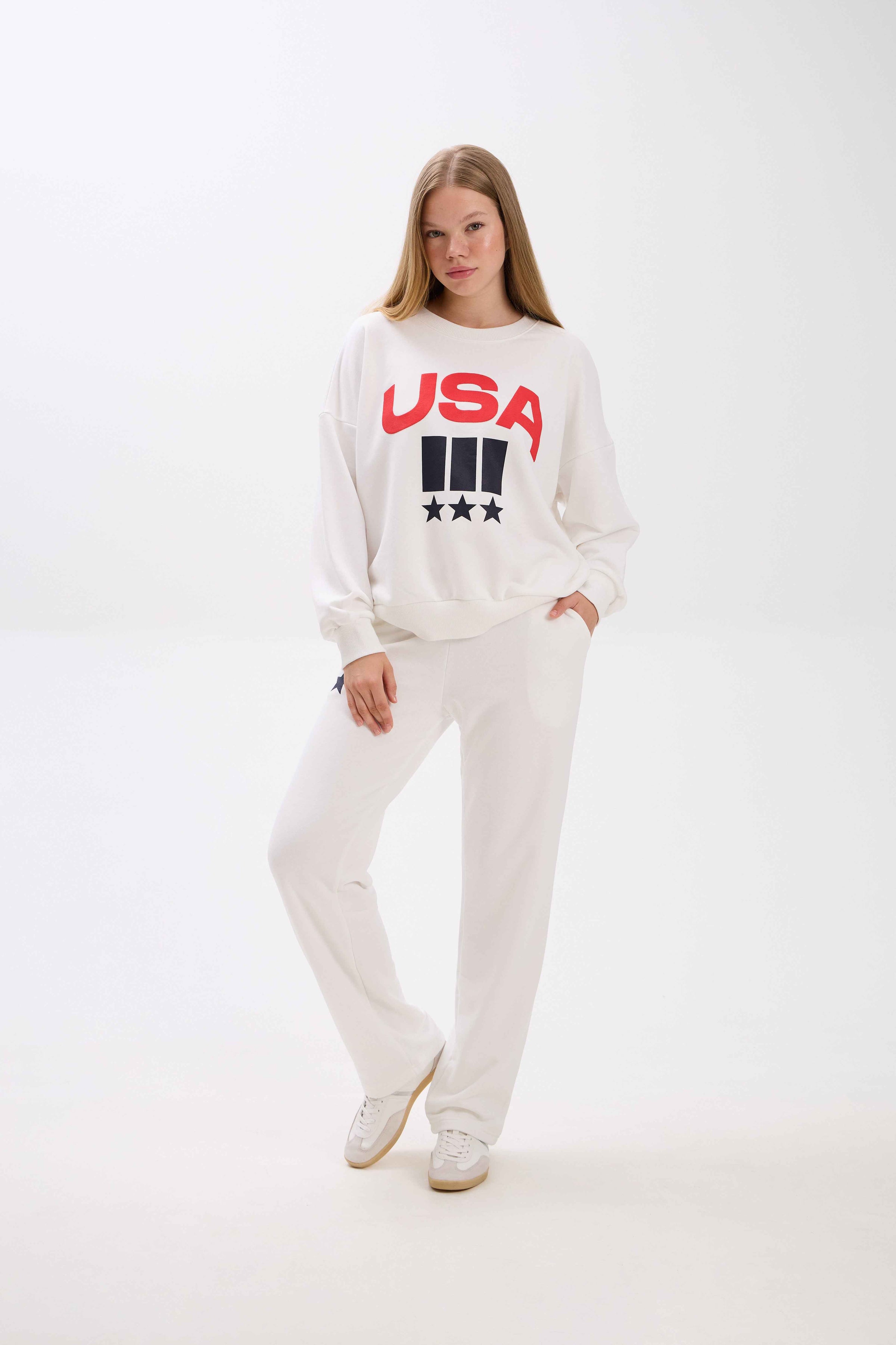 Woman wearing a white sweatshirt with 'USA' text on a white background.