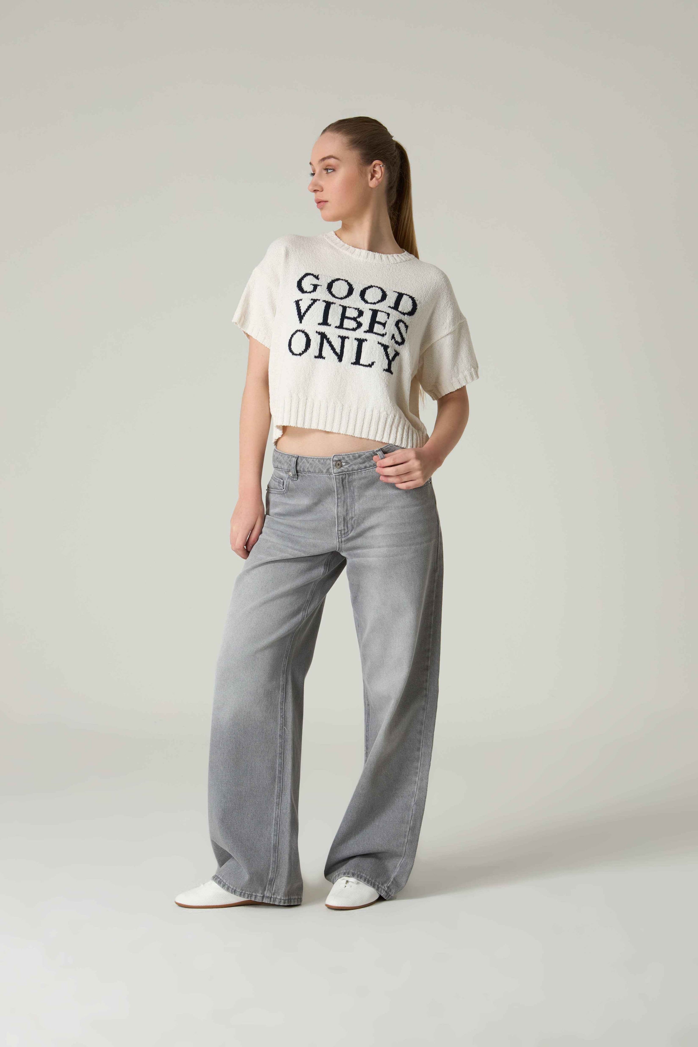 Person wearing a 'Good Vibes Only' t-shirt and gray pants on a plain background.