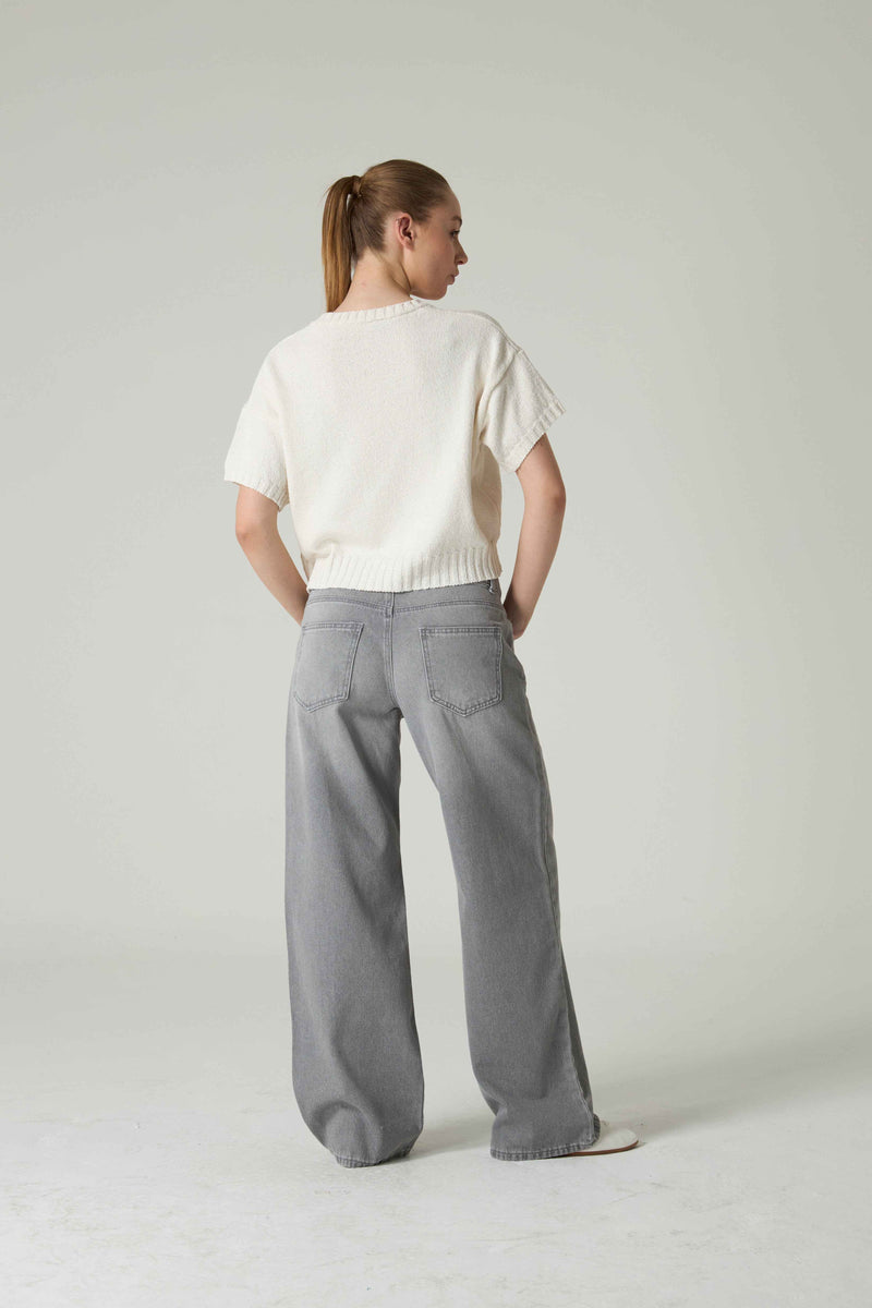 Person wearing a white top and gray pants on a plain background.