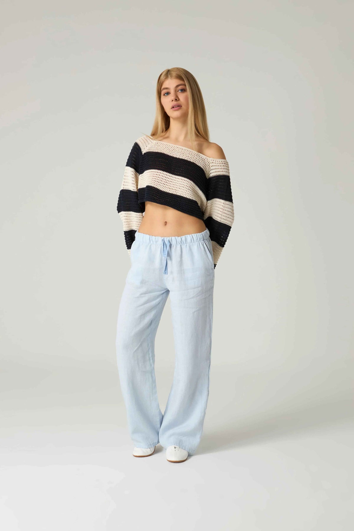 Woman wearing a black and white striped sweater and light blue pants on a plain background.