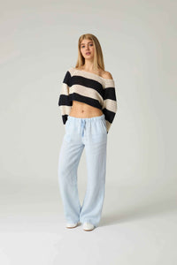 Woman wearing a black and white striped sweater and light blue pants on a plain background.