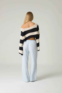 Person wearing a black and white striped sweater and light blue pants on a plain background.