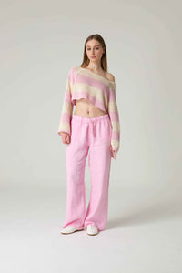 Woman wearing a striped off-shoulder top and pink pants on a white background.