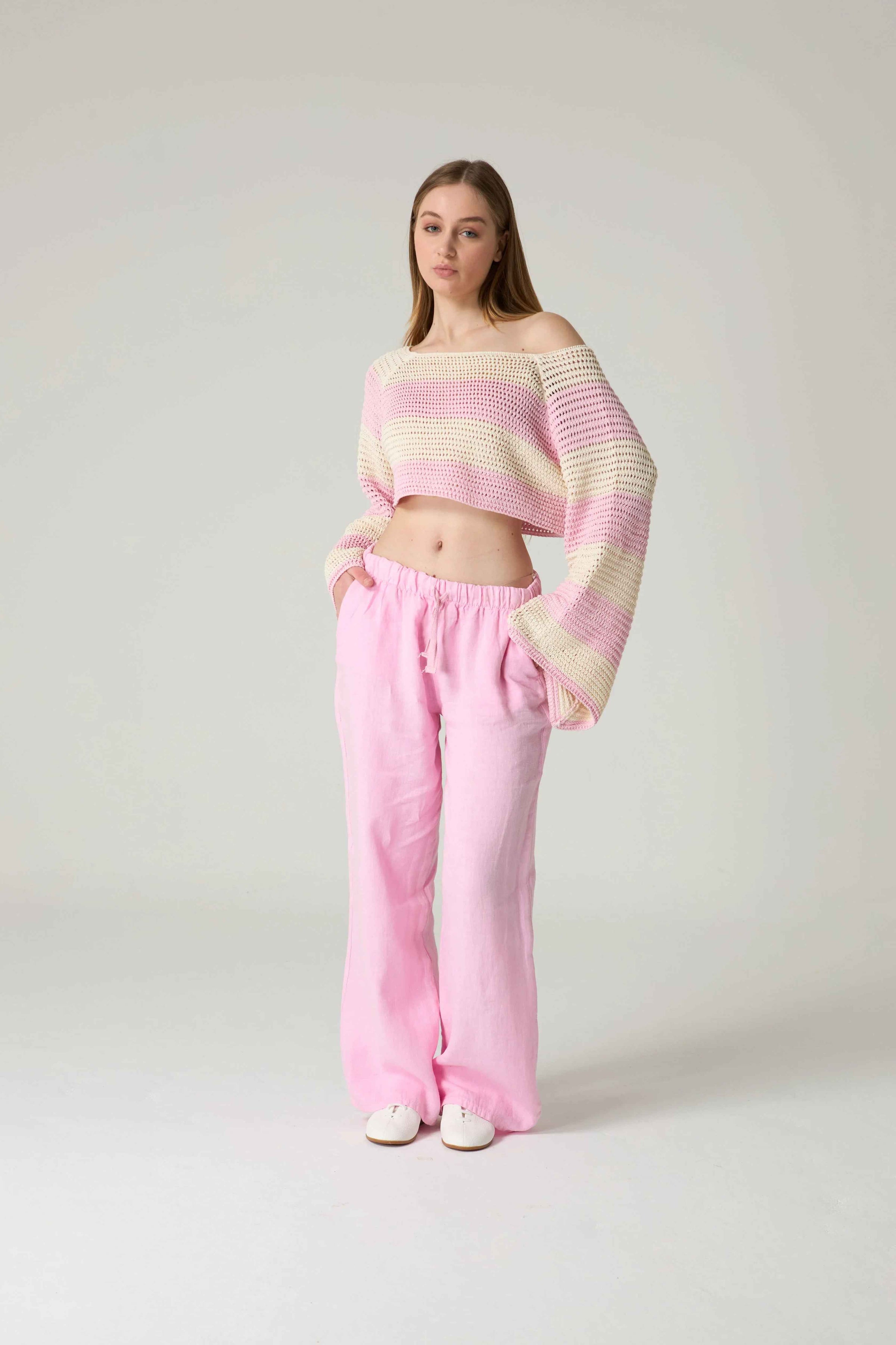 Woman wearing a striped sweater and pink pants on a white background.