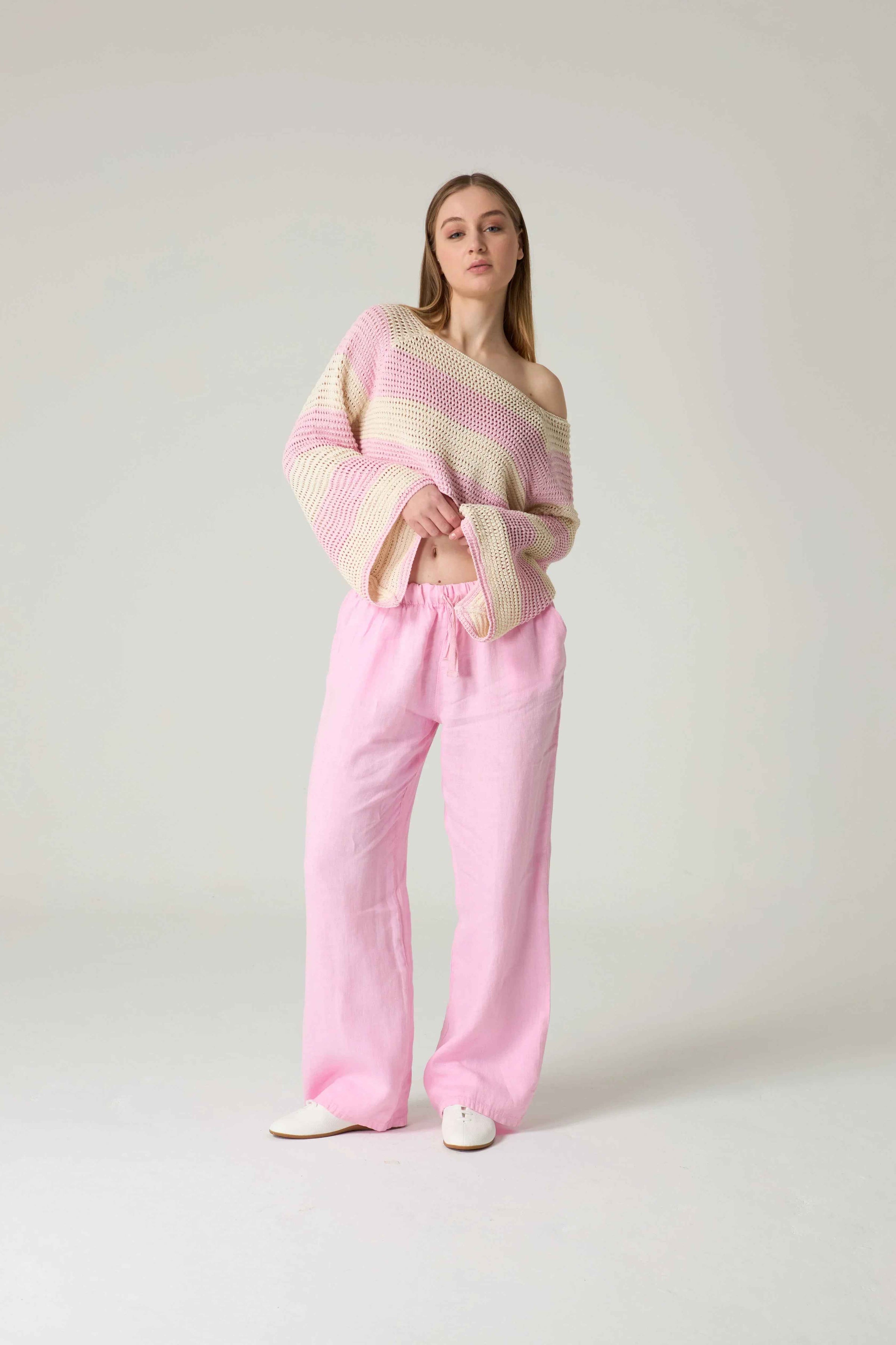 Woman wearing a striped sweater and pink pants on a white background.