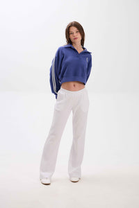 Person wearing a blue cropped sweatshirt with white stripes and white pants on a white background.