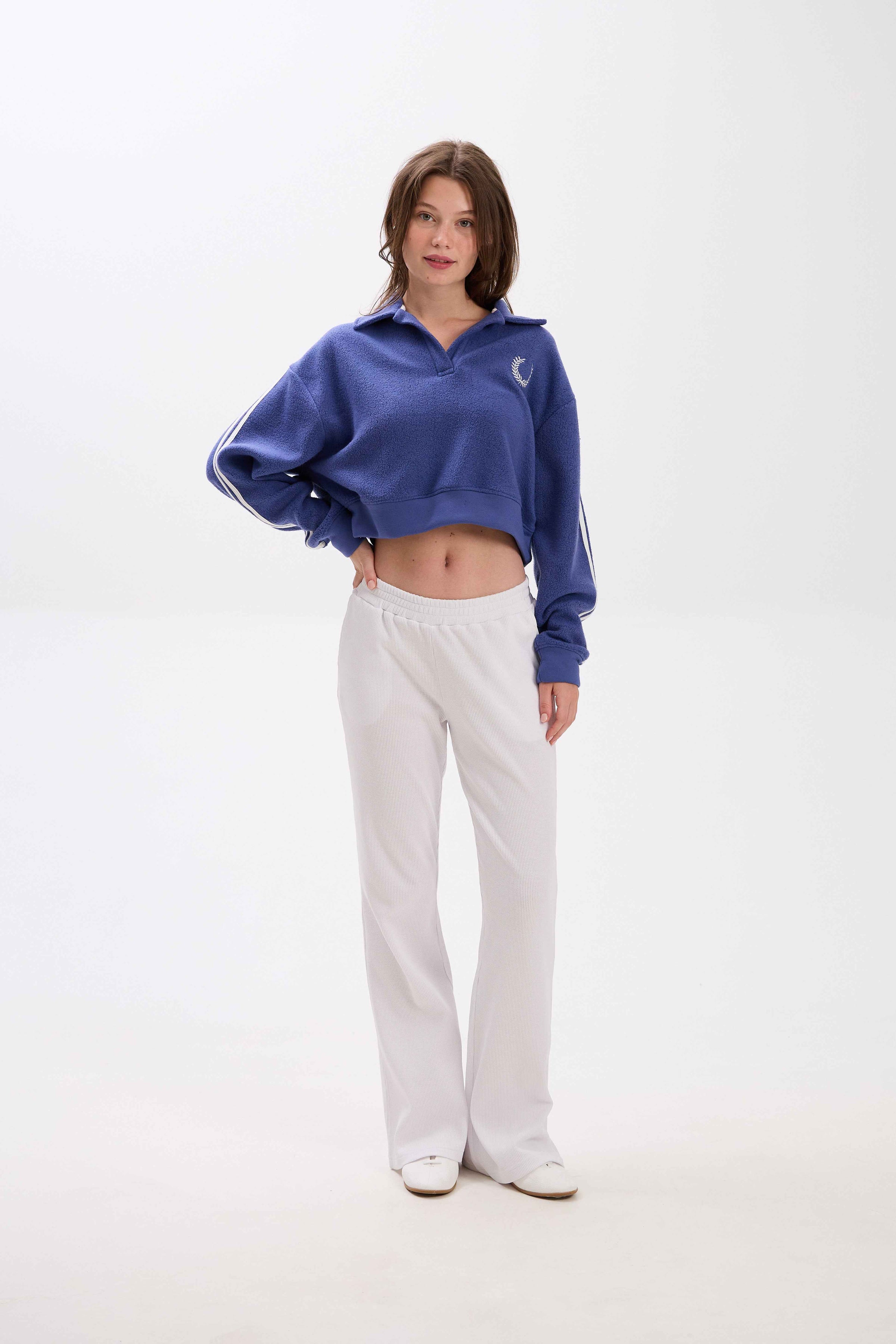 Person wearing a blue cropped jacket and white pants on a white background.