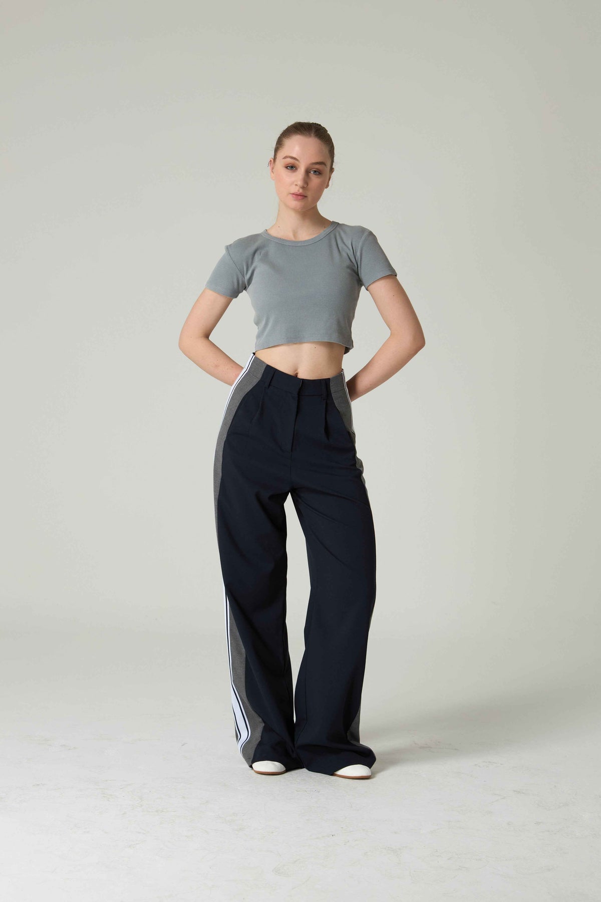 Person wearing a gray crop top and black pants on a plain background.