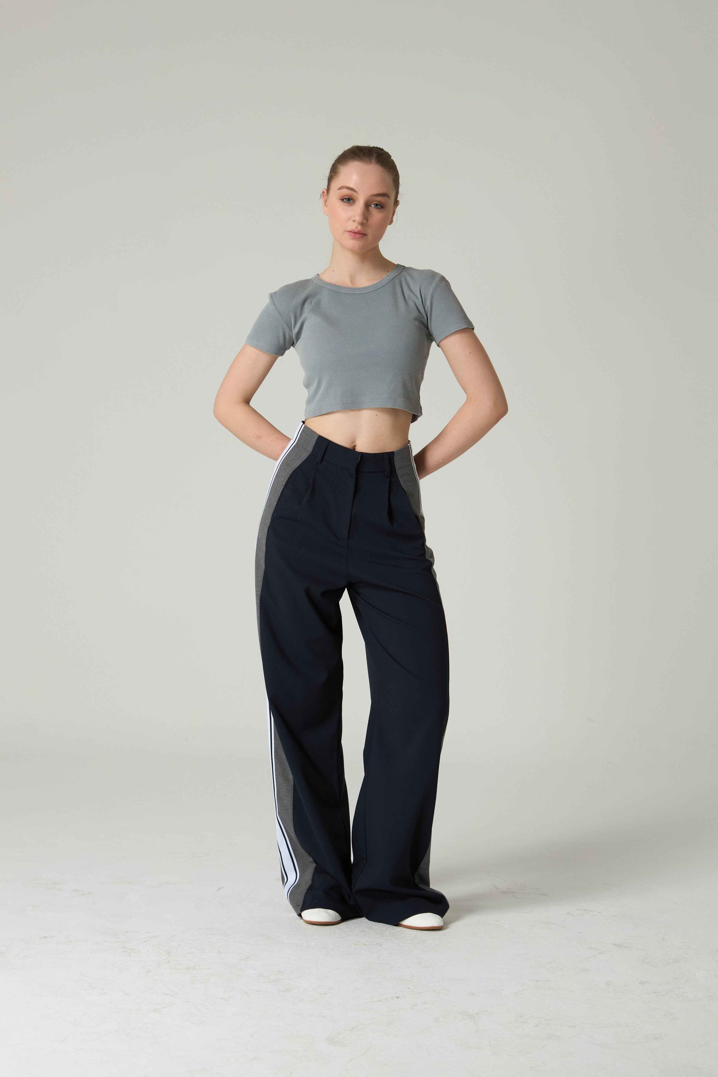 Person wearing a gray crop top and black pants on a plain background.