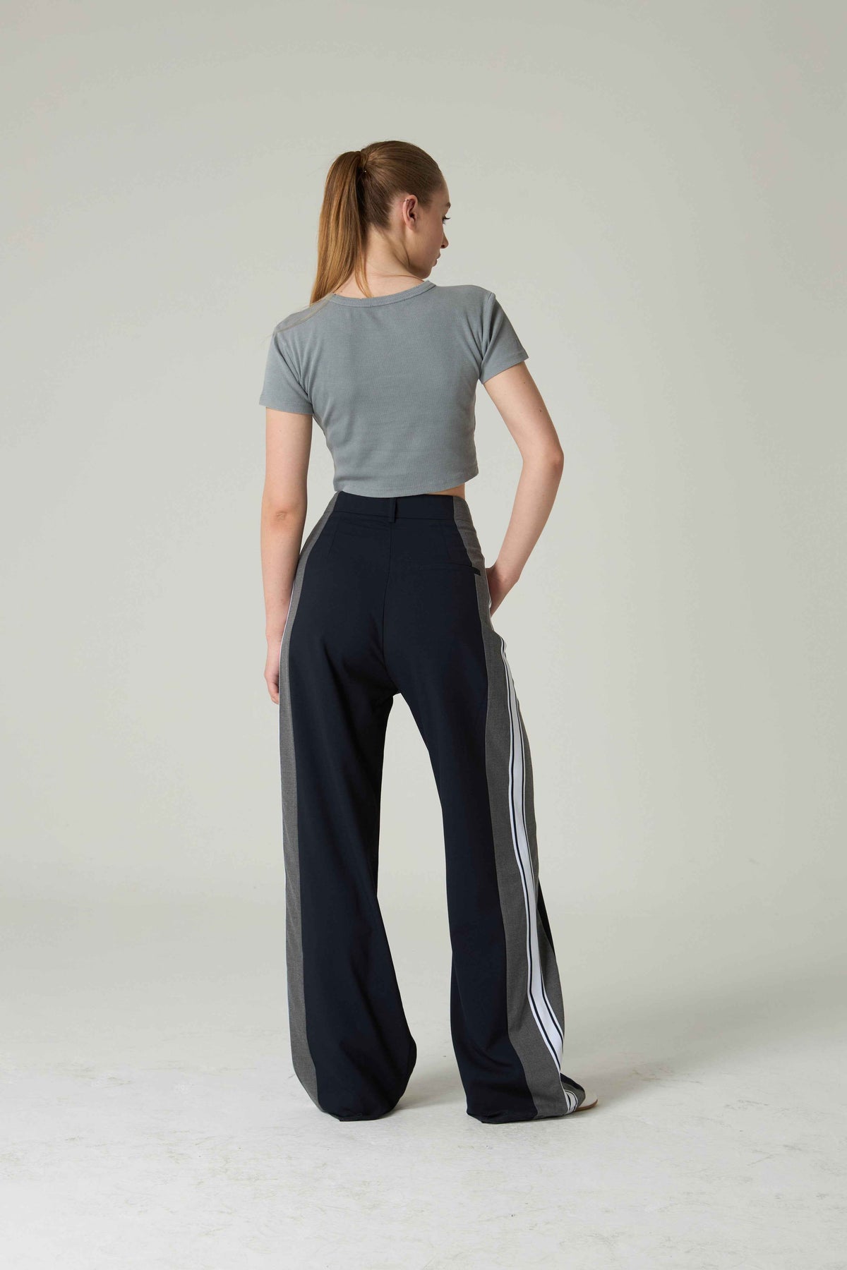 Woman wearing a gray crop top and black pants with white stripes on a plain background.