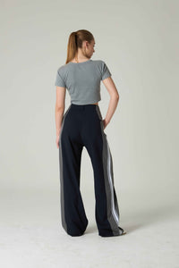 Woman wearing a gray crop top and black pants with white stripes on a plain background.