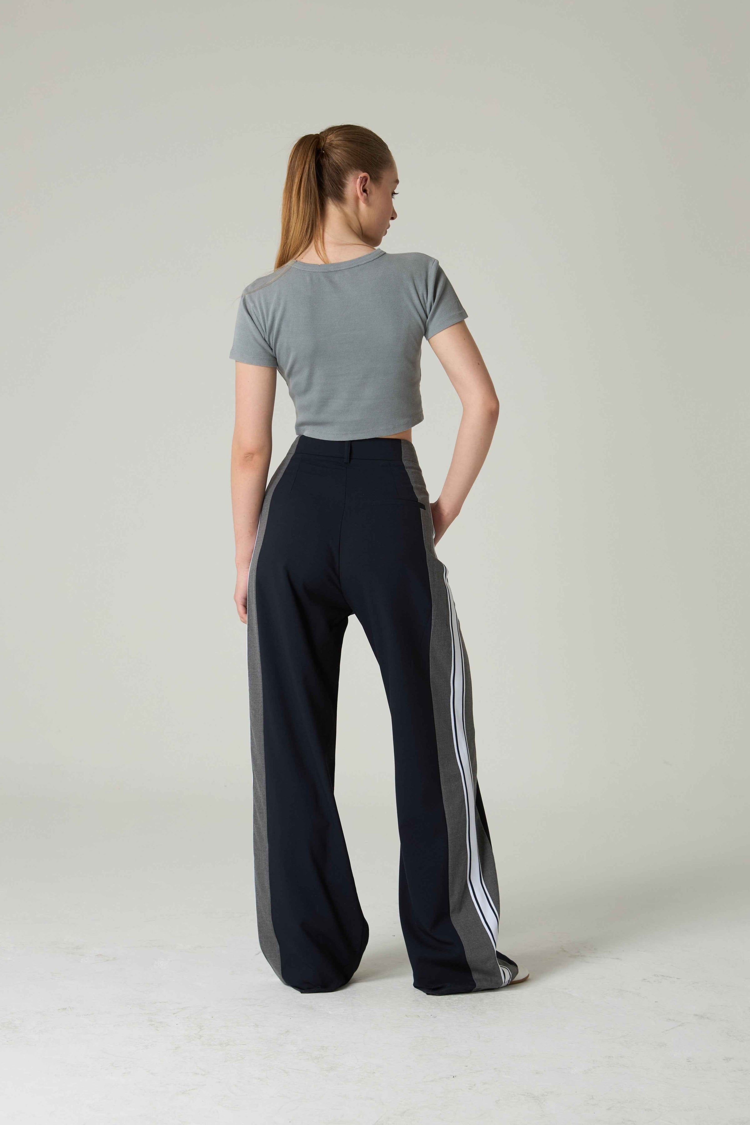 Woman wearing a gray crop top and black pants with white stripes on a plain background.