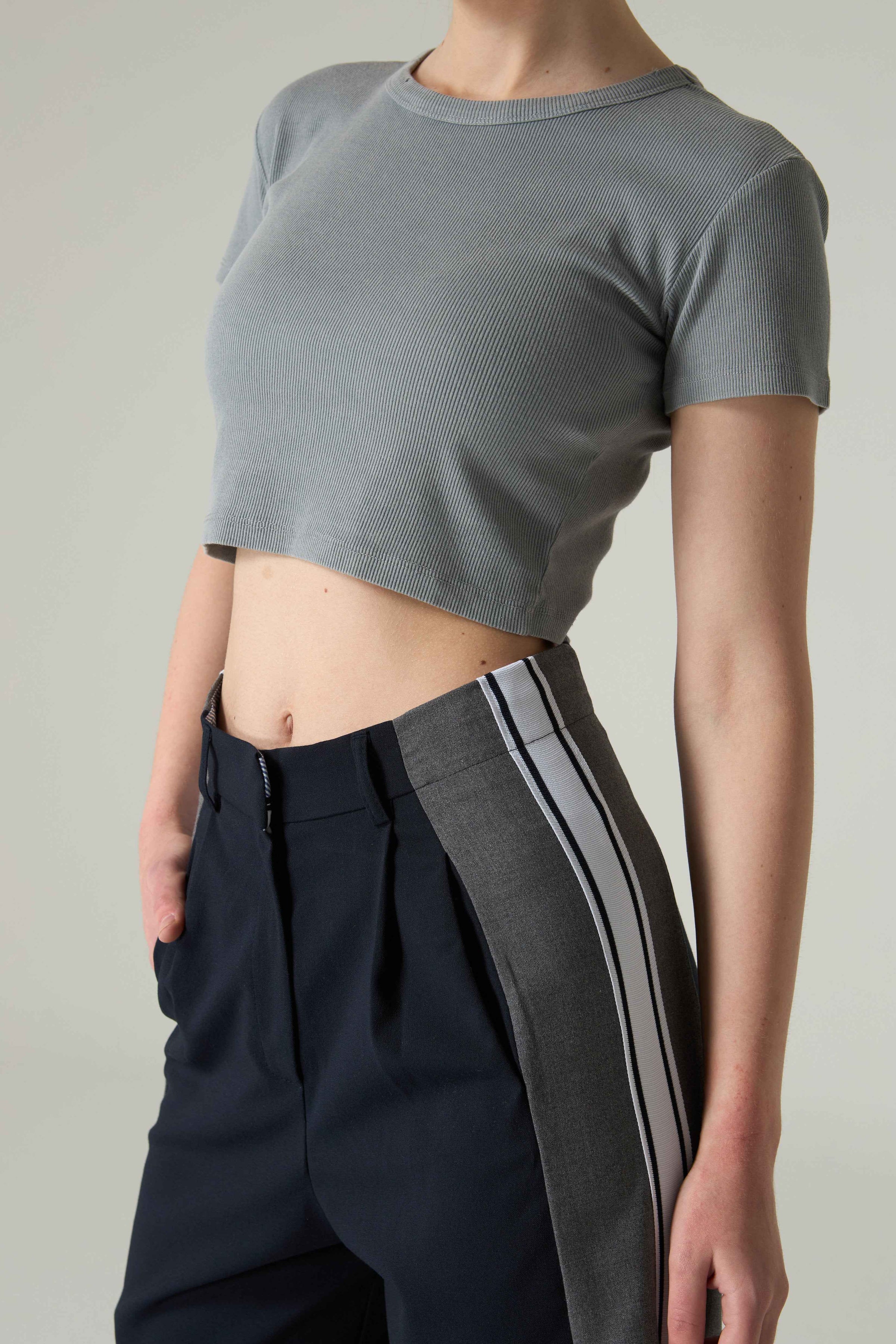 Person wearing a gray cropped t-shirt and black pants with a stripe on a neutral background.