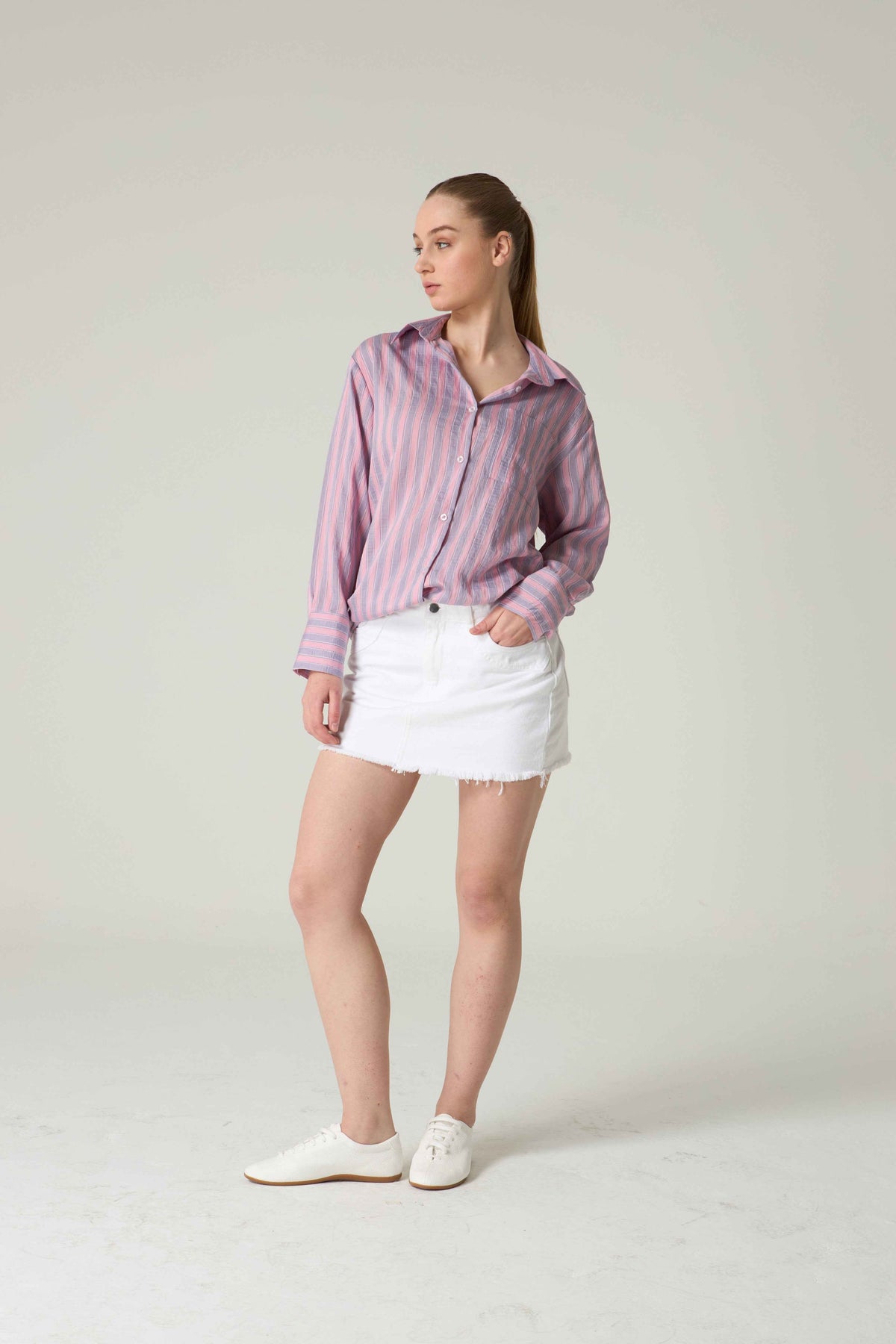 Woman wearing a pink striped shirt and white skirt on a plain background.