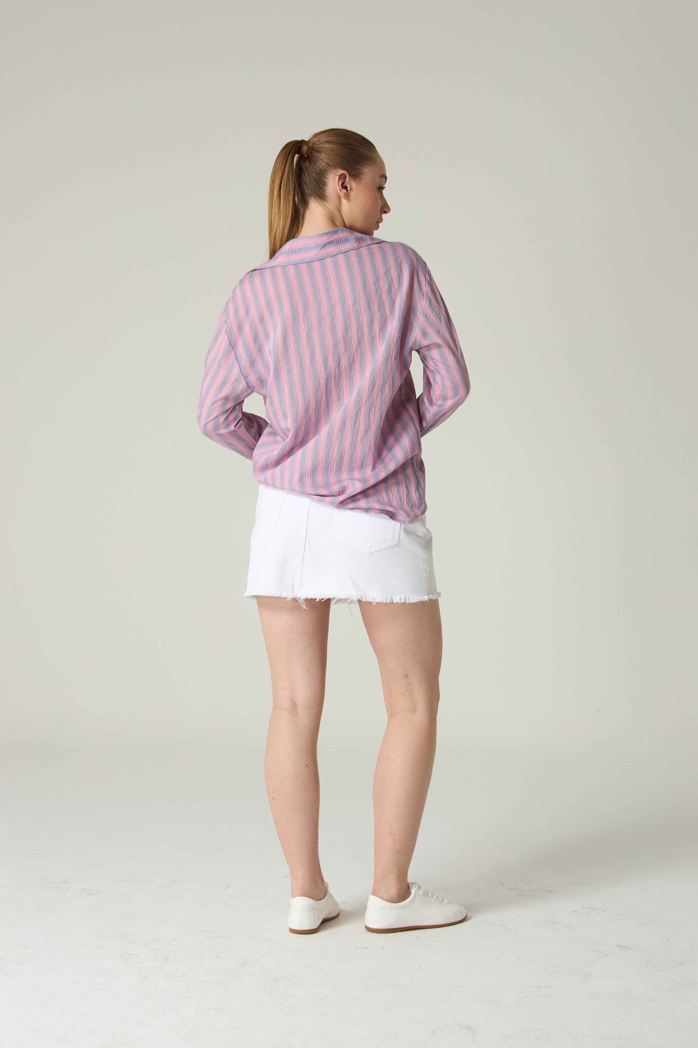 Person wearing a pink and white striped shirt with a white skirt on a plain background.