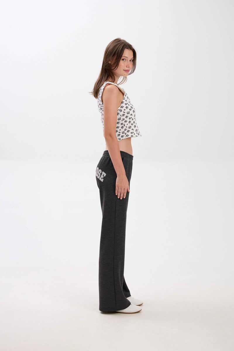 Woman wearing a patterned top and black pants on a white background.