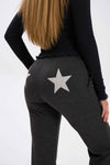 Person wearing dark gray jogger pants with a star design on the back, on a white background..