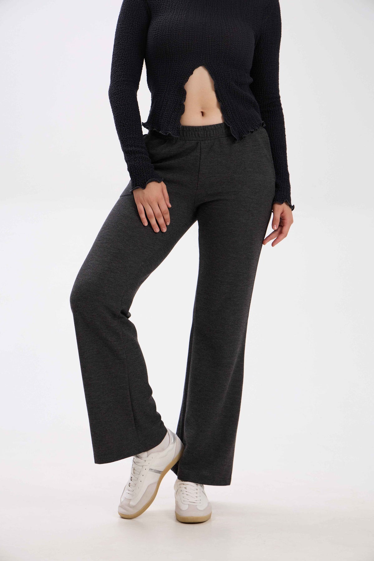 Person wearing black long-sleeve top and dark gray flared pants on a white background.